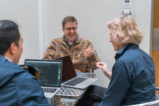 A photograph of a group of people sitting around a table with their laptops.