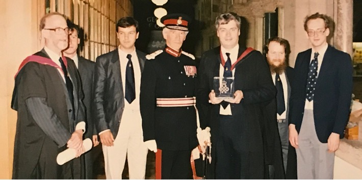 A group photo of 7 men standing: left to right: Tony Hoare, Tony Cox, Geoff Barrett, Sir Ashley Ponsonby (Lord Lieutenant at the time), Bill Roscoe, Michael Goldsmith and David Shepherd at the presentation of the Queen's Award for Technology in 1990