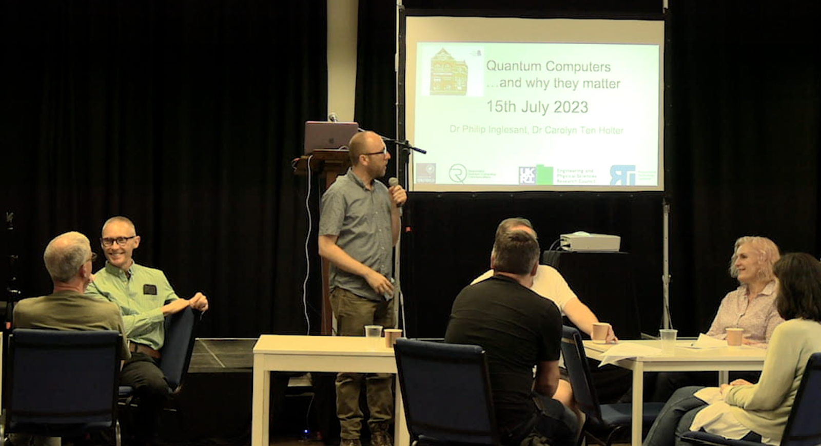 Image showing one of the community lab events at the Upper Norwood Library Hub, with a speaker and attendees, and a large projector screen in the background.