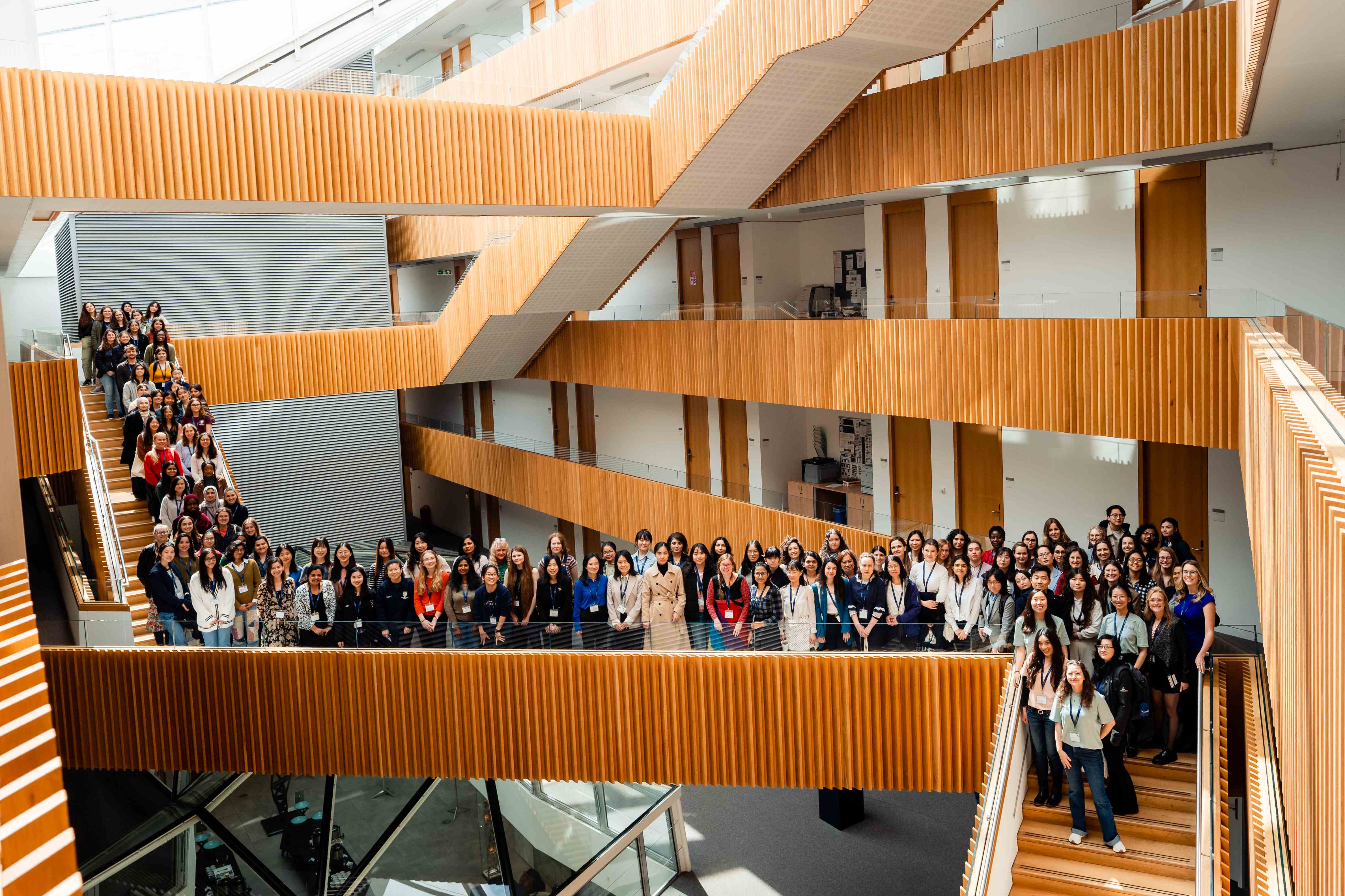 Photo shows all attendees of the Oxbridge Women in CS event, gathered on the stairwells and balconies above the atrium of the Maths Institute&nbsp;