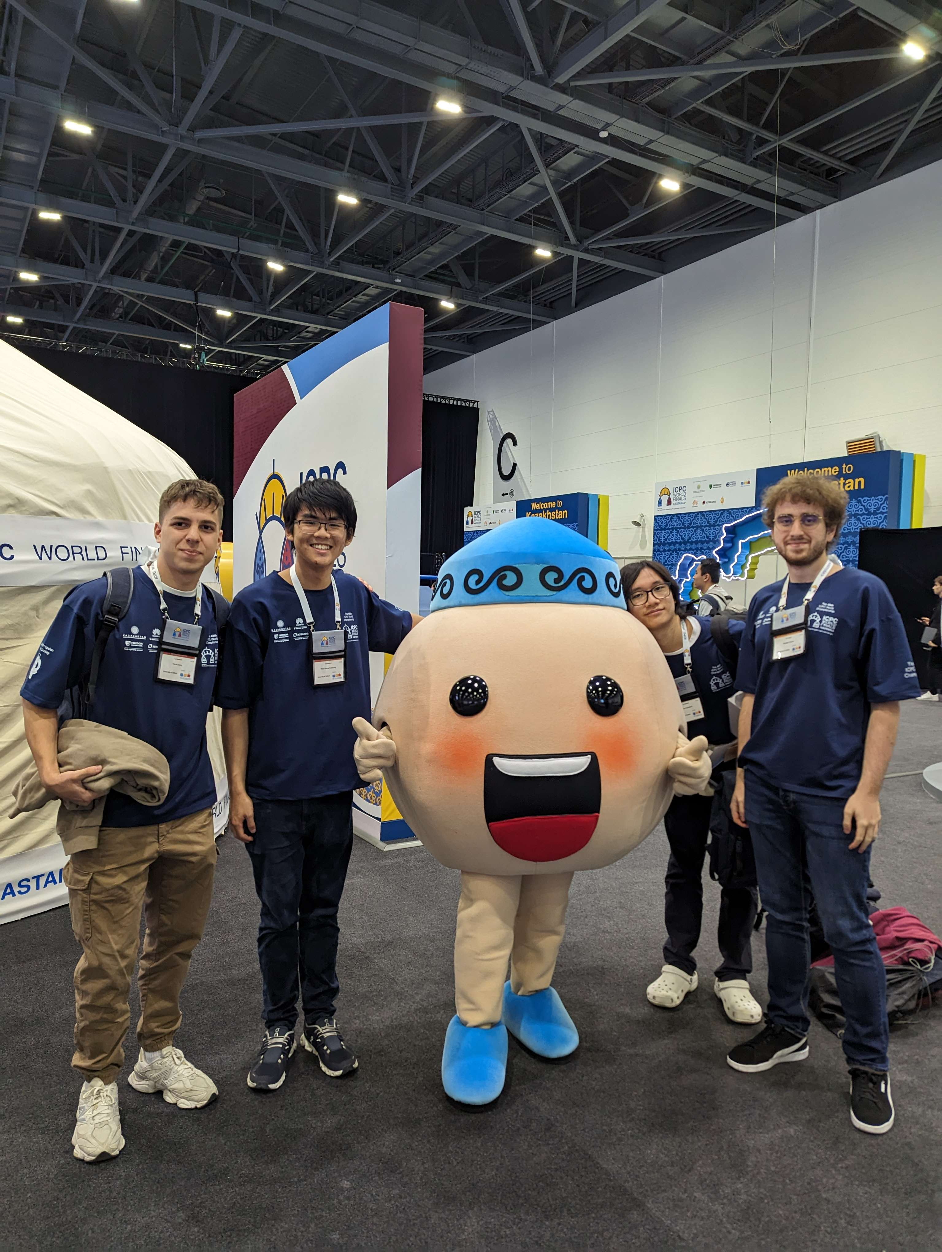 Photo showing competition entrants Viktor, Thien, Harris, and acting coach Radostin Chonev (l-r), posing with the event mascot.